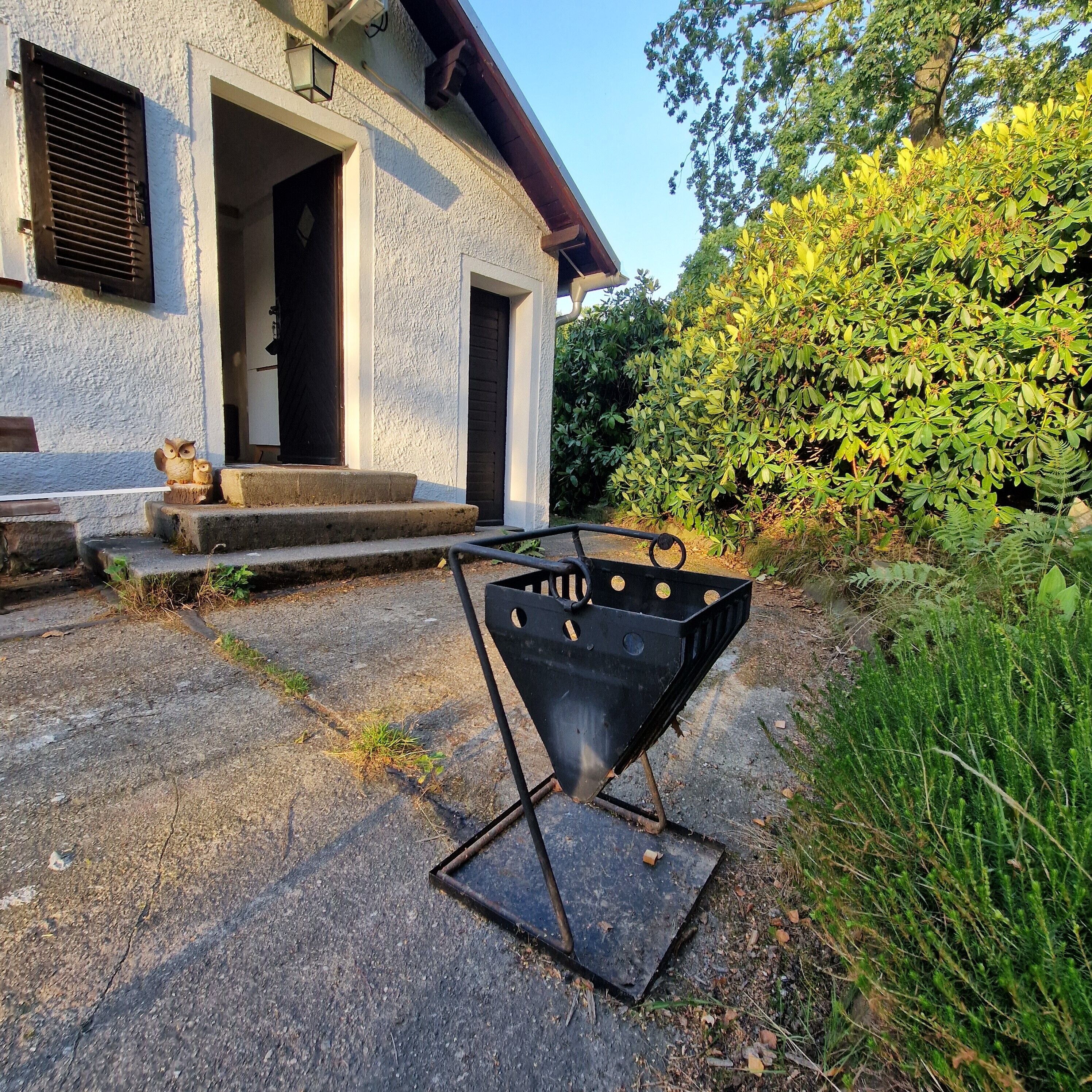 Ein Haus mit einer Beton-Terrasse, einem Metallgrill und einer Holzbank mit Eulenverziierung.