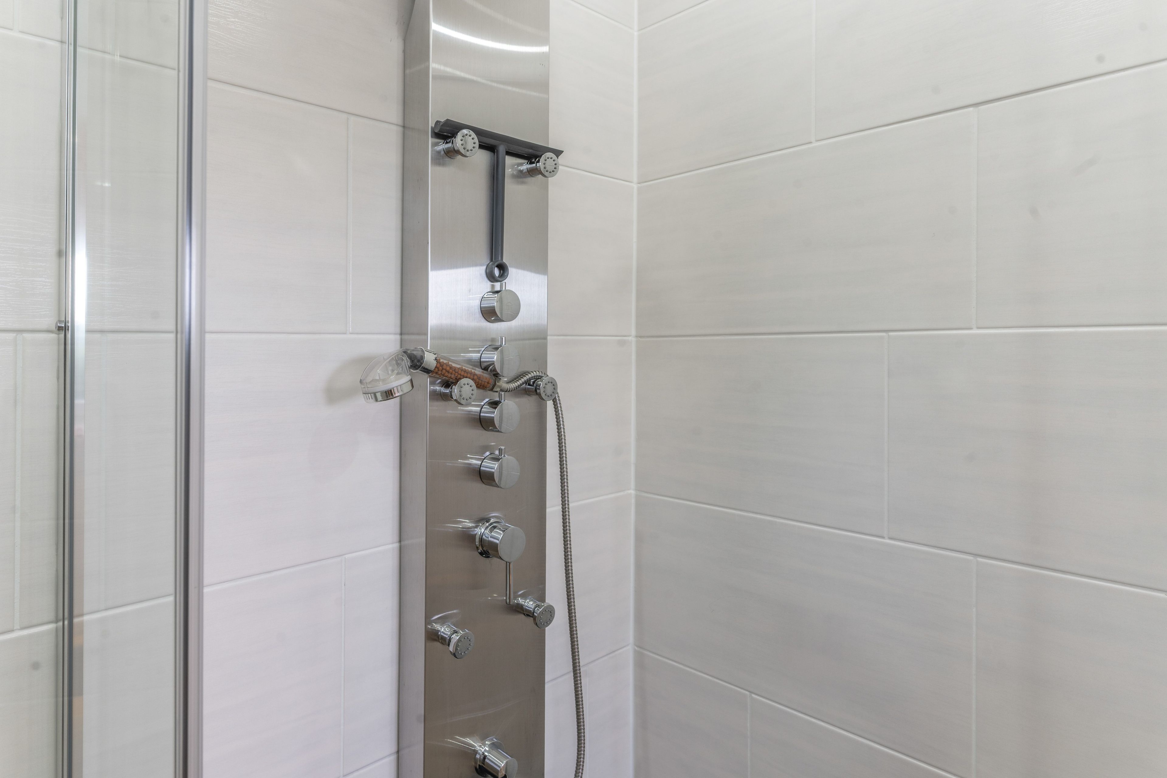 Eine Dusche mit mehreren chromfarbenen Armaturen, darunter ein Handbrausegerät und ein am Wand montierter Wasserhahn.
