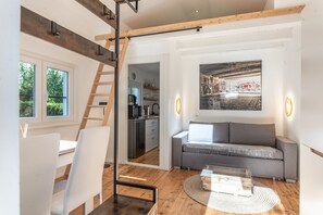 Un intérieur moderne comprenant un escalier, un canapé, un coin repas et une cuisine visible à travers une porte ouverte.