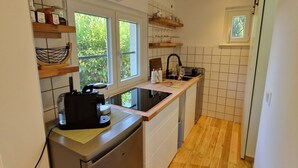 Et kompakt køkken med opvaskemaskine, kaffemaskine og et vindue, der giver naturligt lys.
