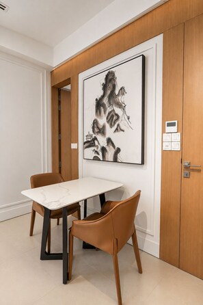 Una habitación con una mesa de mármol blanco, sillas de cuero marrón, una obra de arte enmarcada en la pared y una puerta de madera con termostato digital.