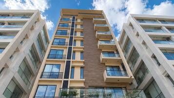 A high-rise building with multiple balconies and large windows, under a partly cloudy sky.