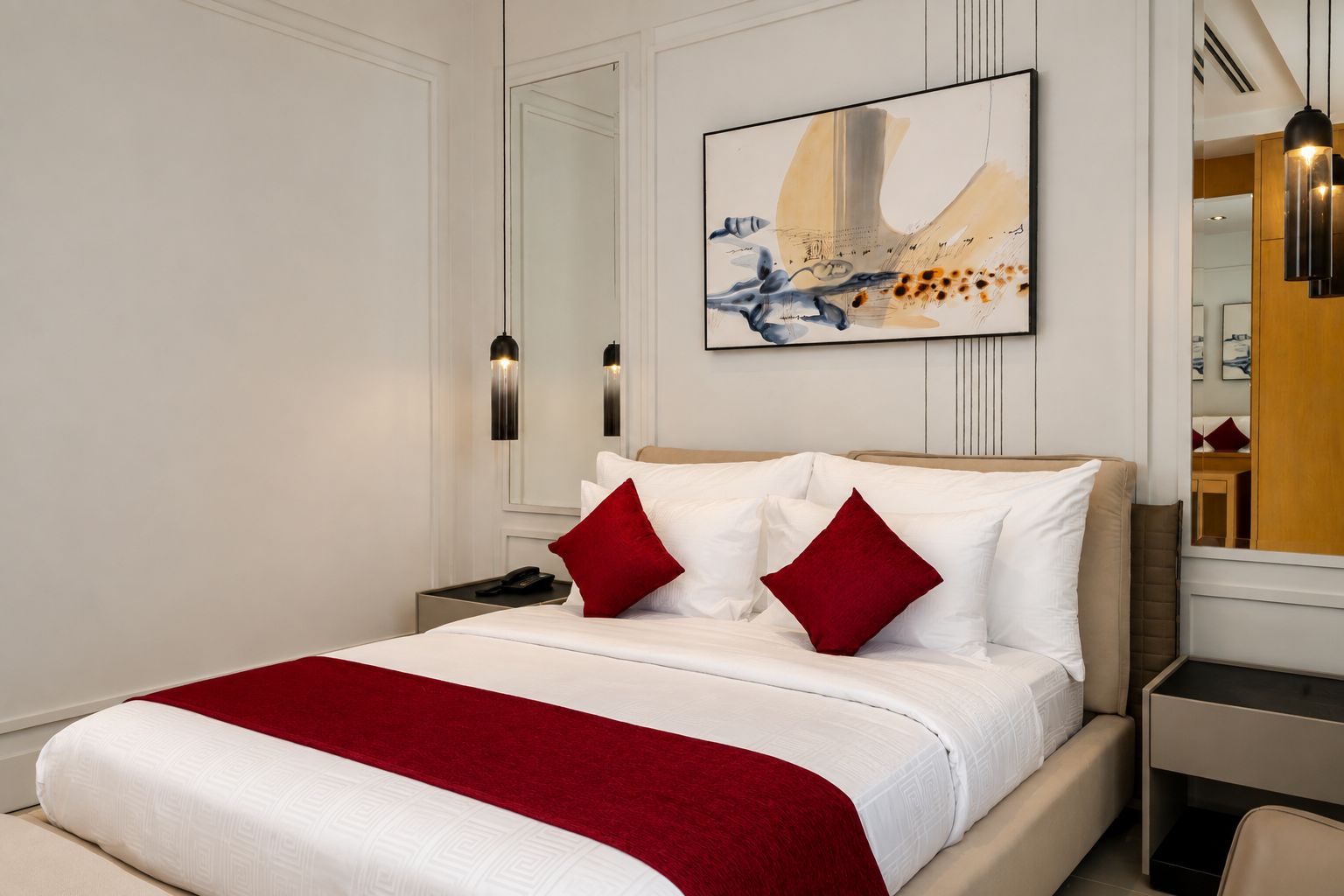 A modern hotel room with a large bed, a red throw blanket, and a painting above the bed.