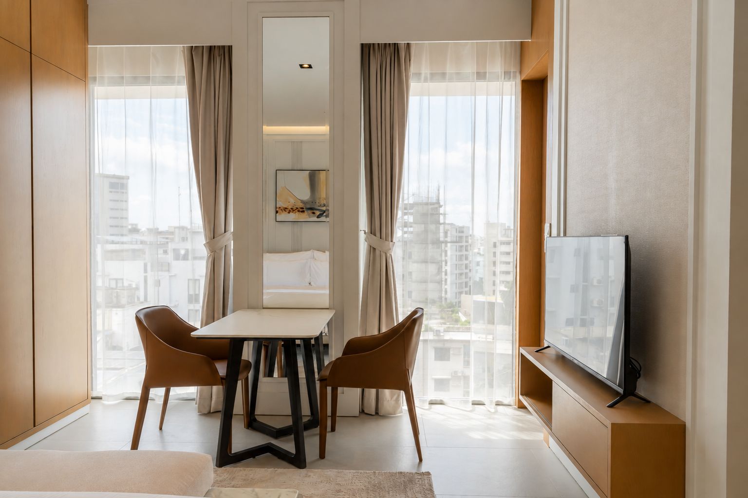 Une chambre d’hôtel équipée d’une table à manger, de deux chaises, d’un téléviseur et offrant une vue sur la ville.