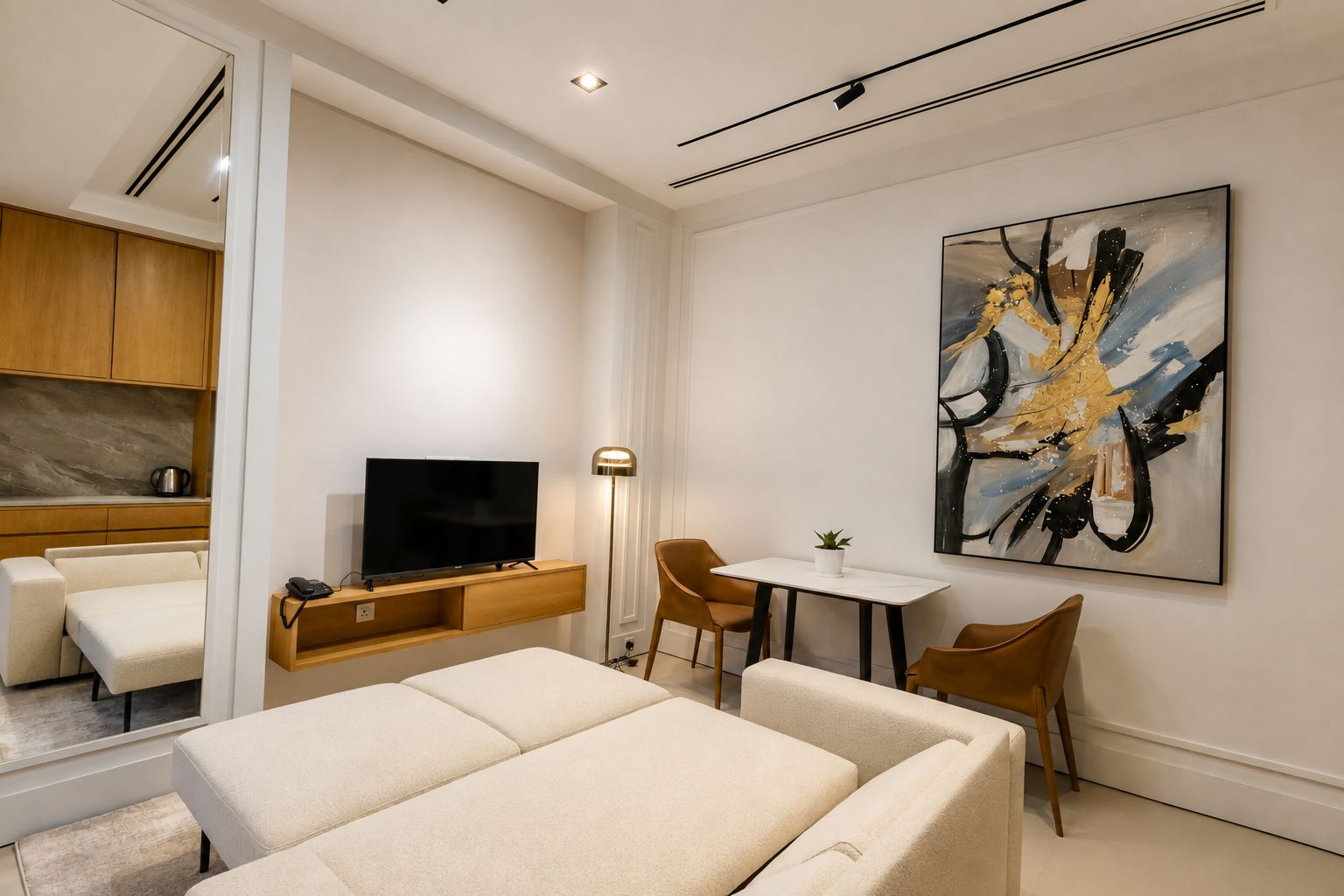 Ein modernes Hotelzimmer mit einem Flachbildfernseher, einer Essecke mit Tisch und Stühlen, einem Sofa und einem großen abstrakten Gemälde an der Wand.