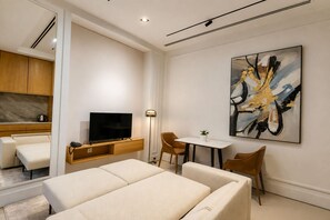 A modern hotel room with a flat-screen TV, a dining area with a table and chairs, a sofa, and a large abstract painting on the wall.