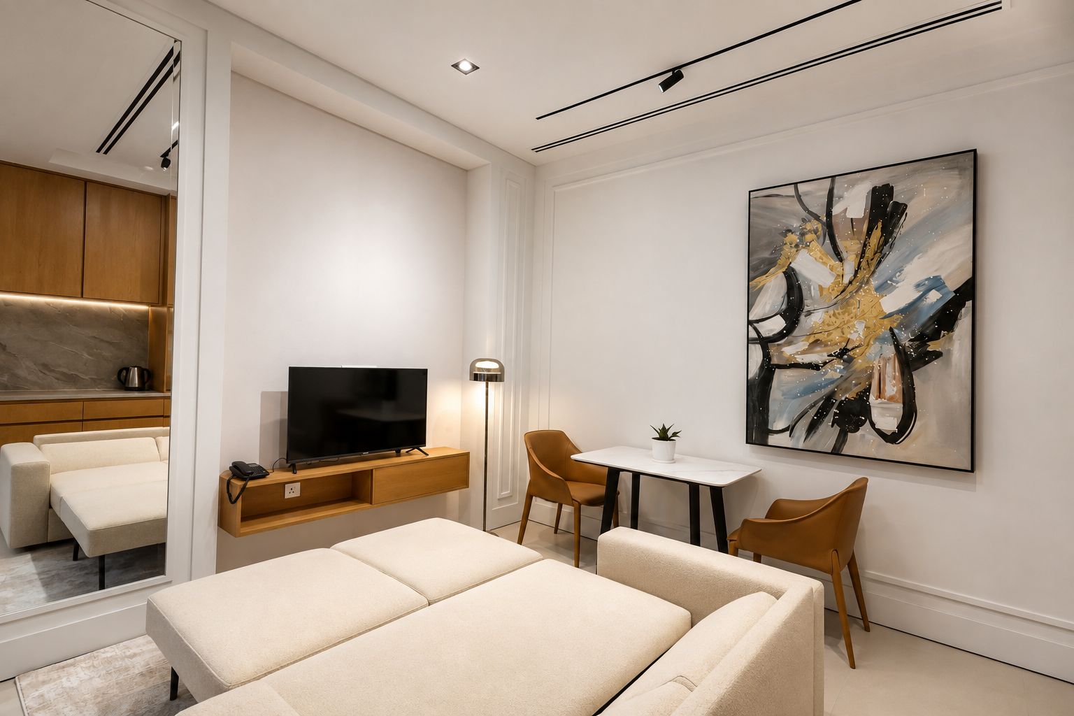 A modern hotel room with a bed, a TV, a desk with chairs, and a large abstract painting on the wall.