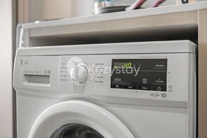 A front view of a white washing machine with a digital display and control panel. - Corvia by Kozystay - Kemayoran (Jakarta Pusat)