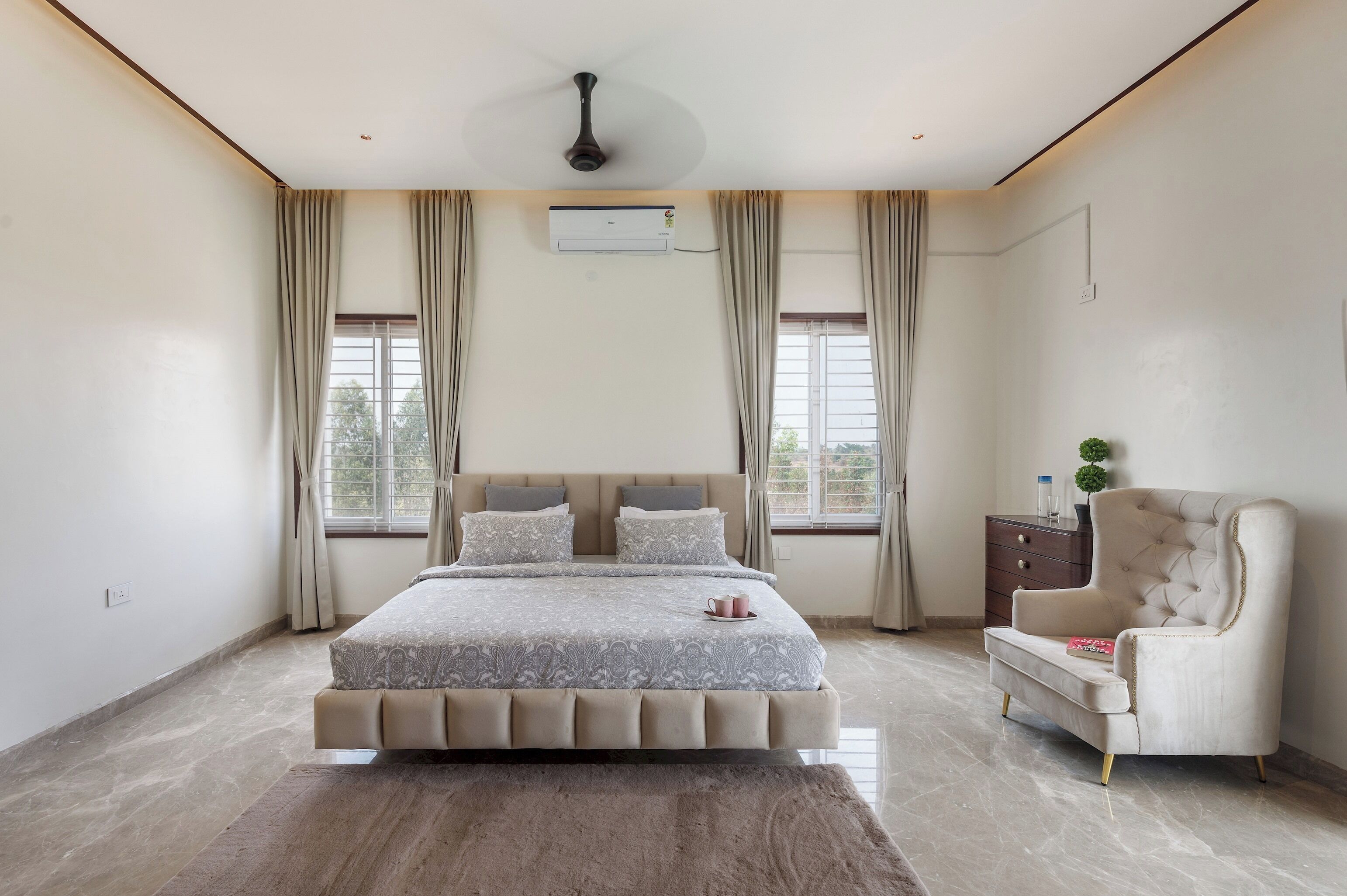 A bedroom with a large bed, a chair, an air conditioning unit, and a window with curtains.