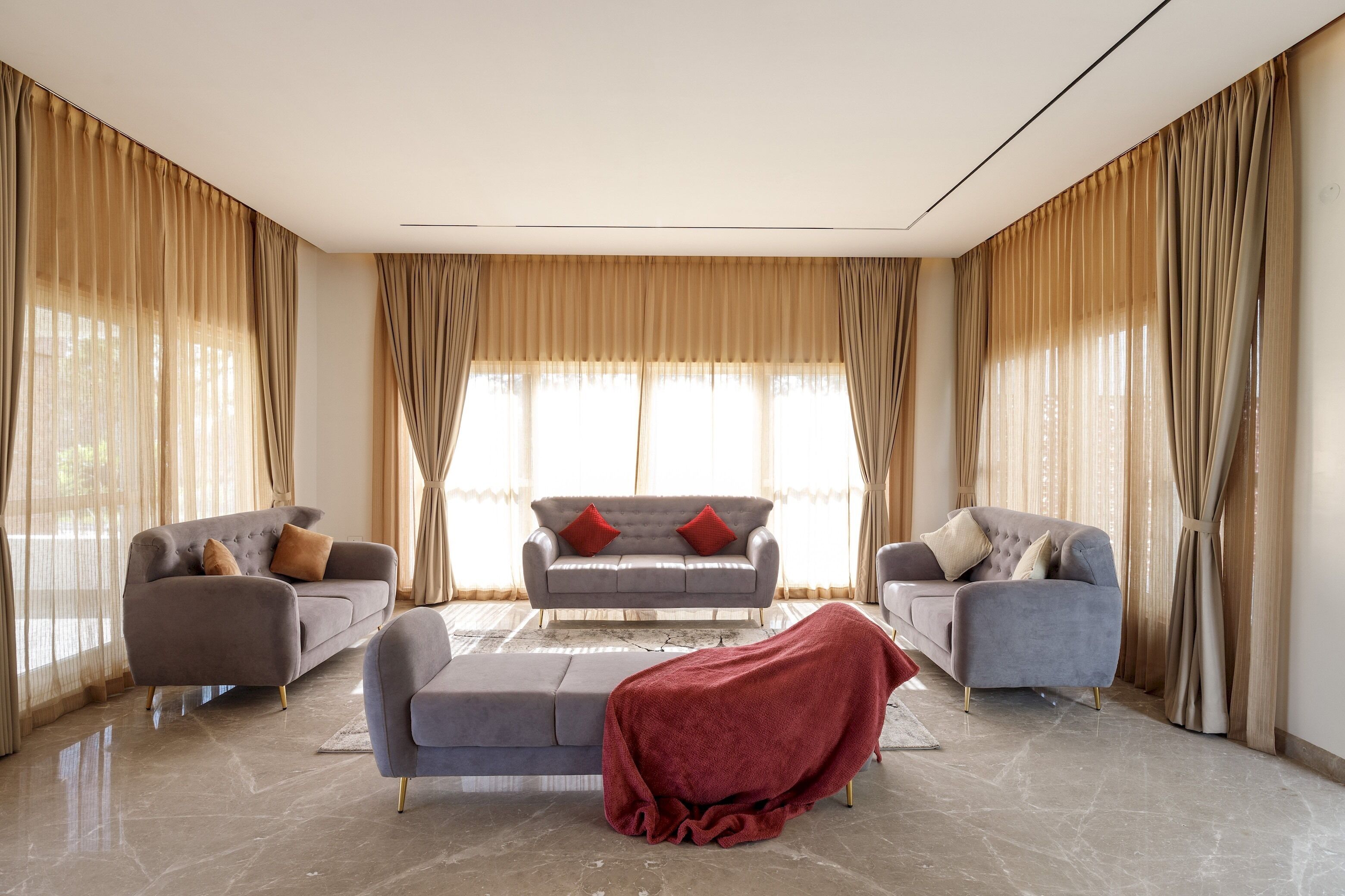 A spacious living room with a grey sofa set, two armchairs, and a red throw blanket on the floor.