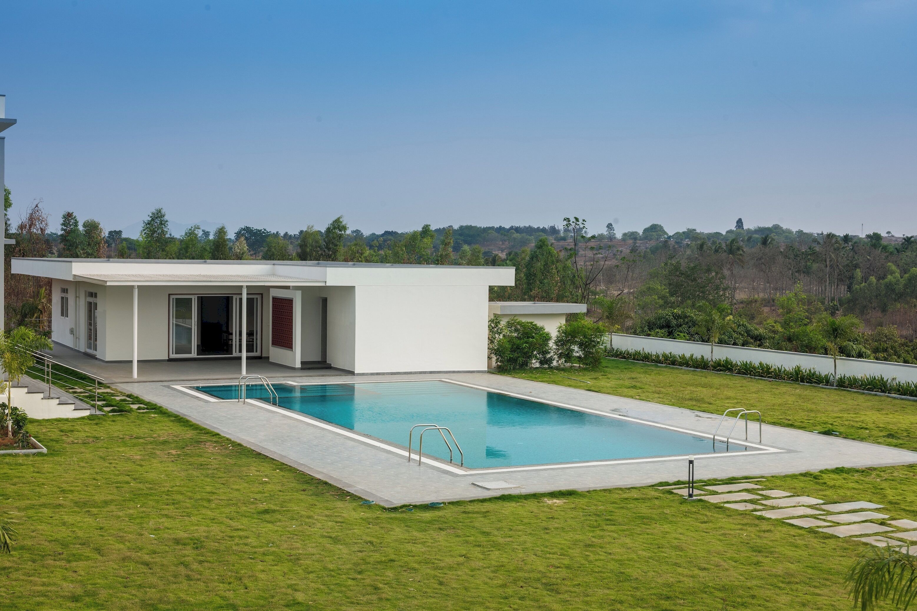 A modern house with a swimming pool, a covered patio, and a view of a hilly landscape.