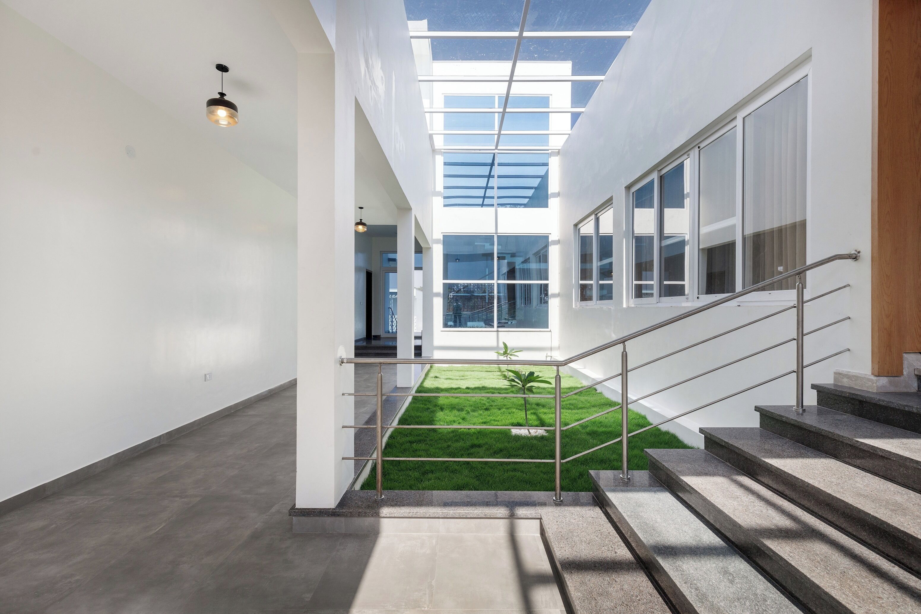 A modern interior with a staircase leading to a glass-enclosed area, a small garden, and a view of the outside.