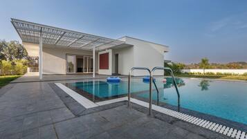 Un'area piscina moderna con una piscina blu cristallina, un portico coperto e vista sul paesaggio circostante.