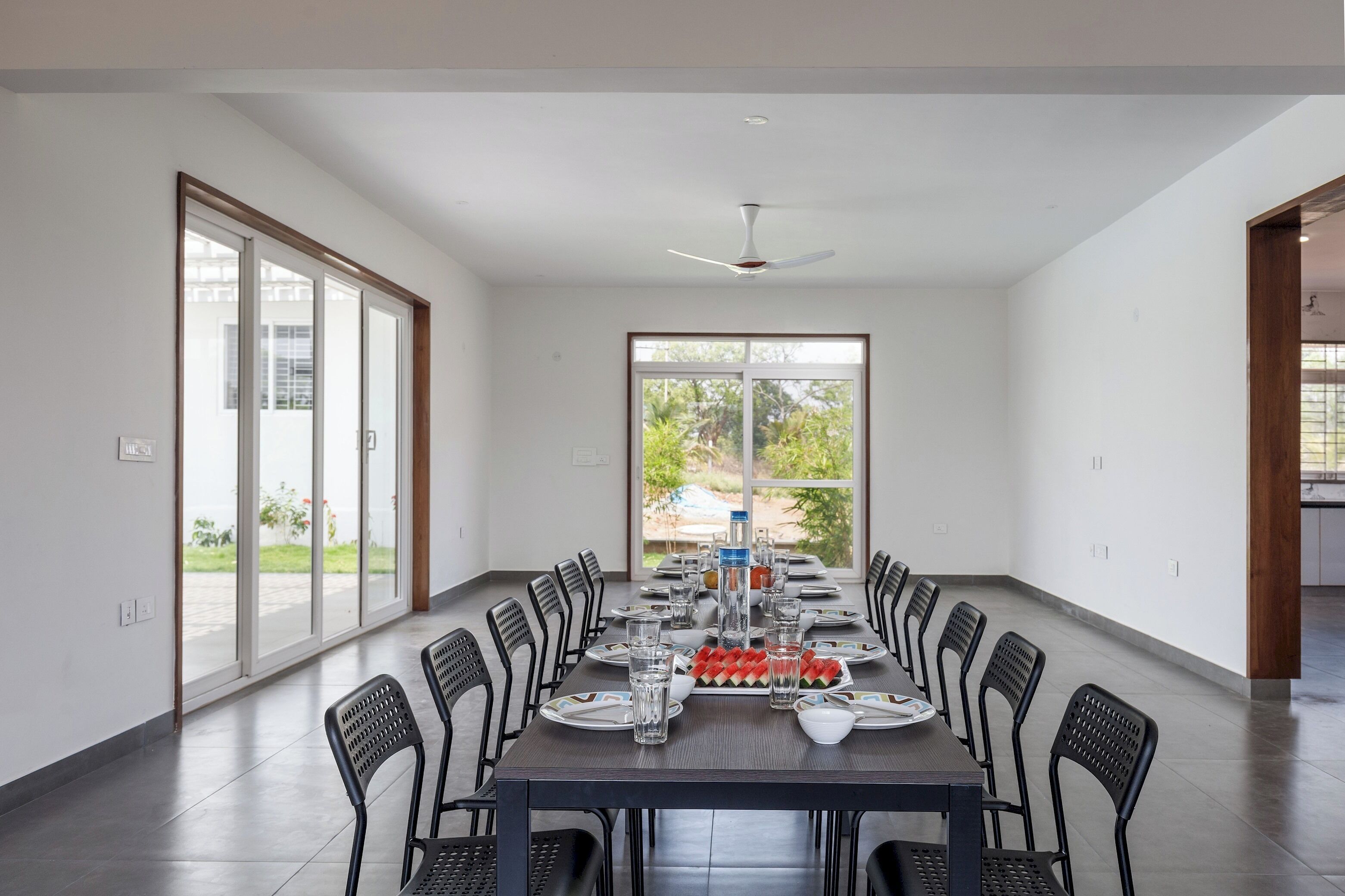A spacious dining area with a long table, chairs, and a view of the outdoors through large windows.