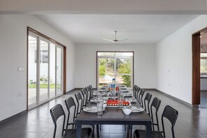 A spacious dining area with a long table, chairs, and a view of the outdoors through large windows.