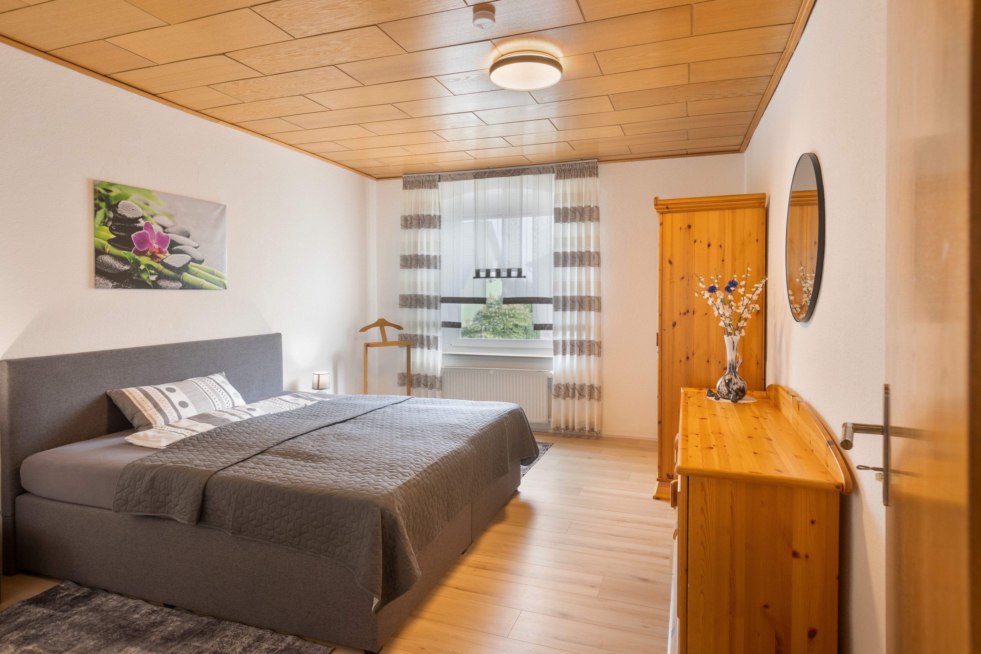 Un dormitorio con una cama, un aparador de madera, un espejo y un cuadro en la pared.