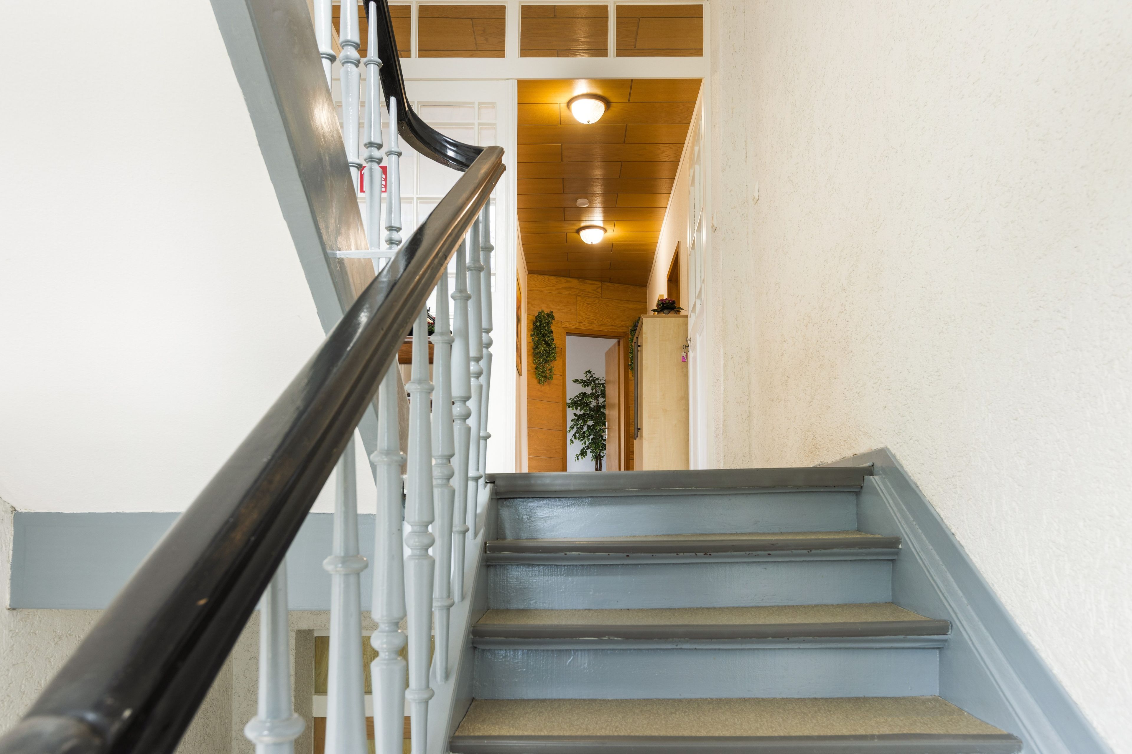 Eine Treppe mit weißen Balustern und einem schwarzen Geländer, das zu einer Holztür führt.