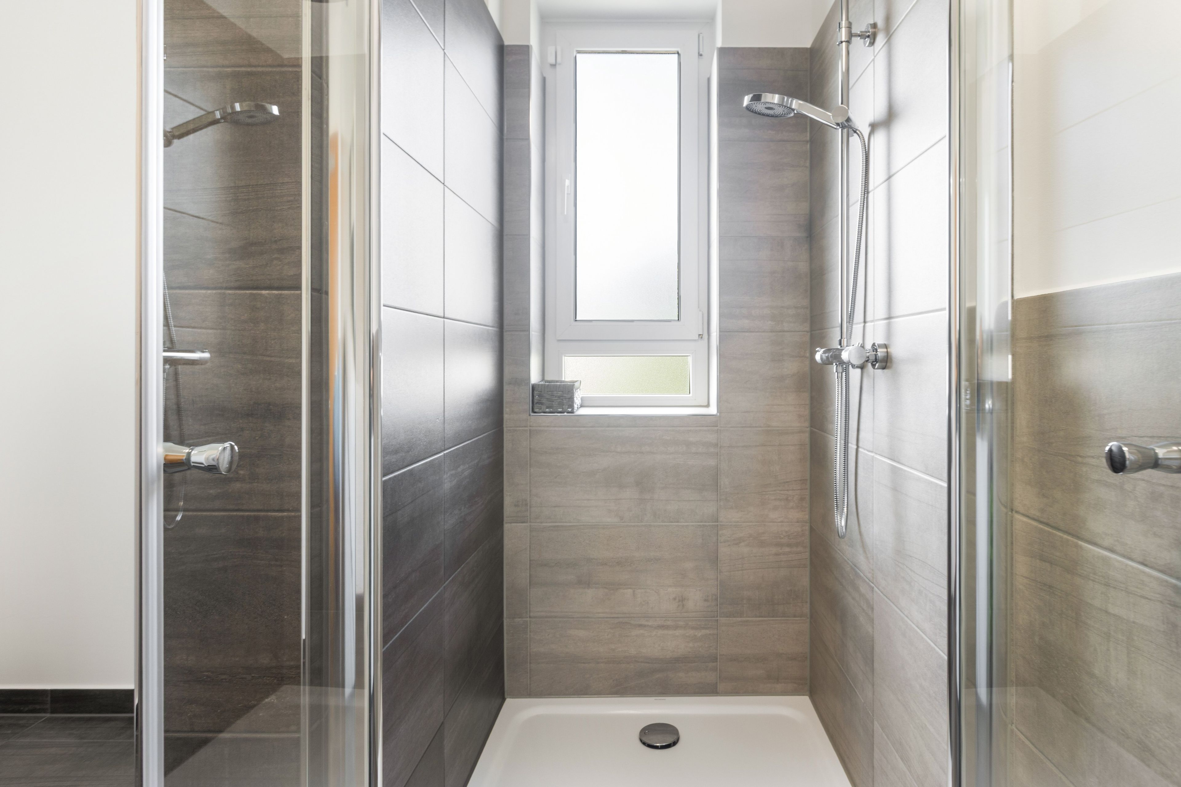 Eine moderne Dusche mit Glastür, Fenster und Duschkopf.