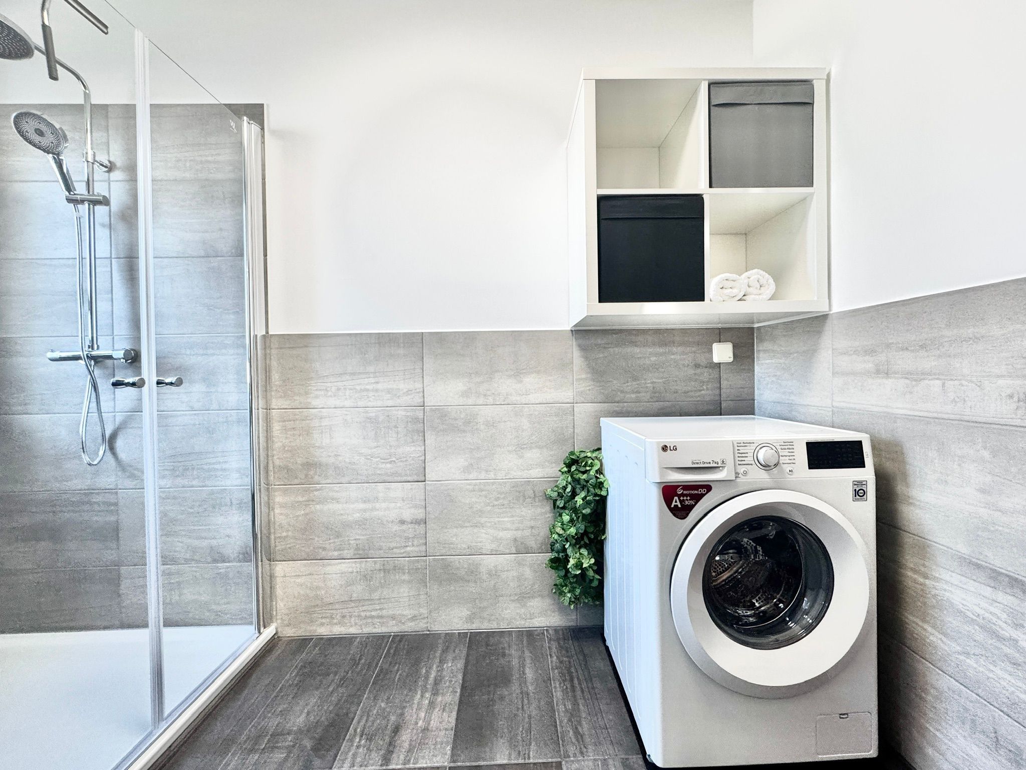 Ein modernes Badezimmer mit Duschkabine aus Glas, integriertem Waschmaschine und einer kleinen Pflanze.