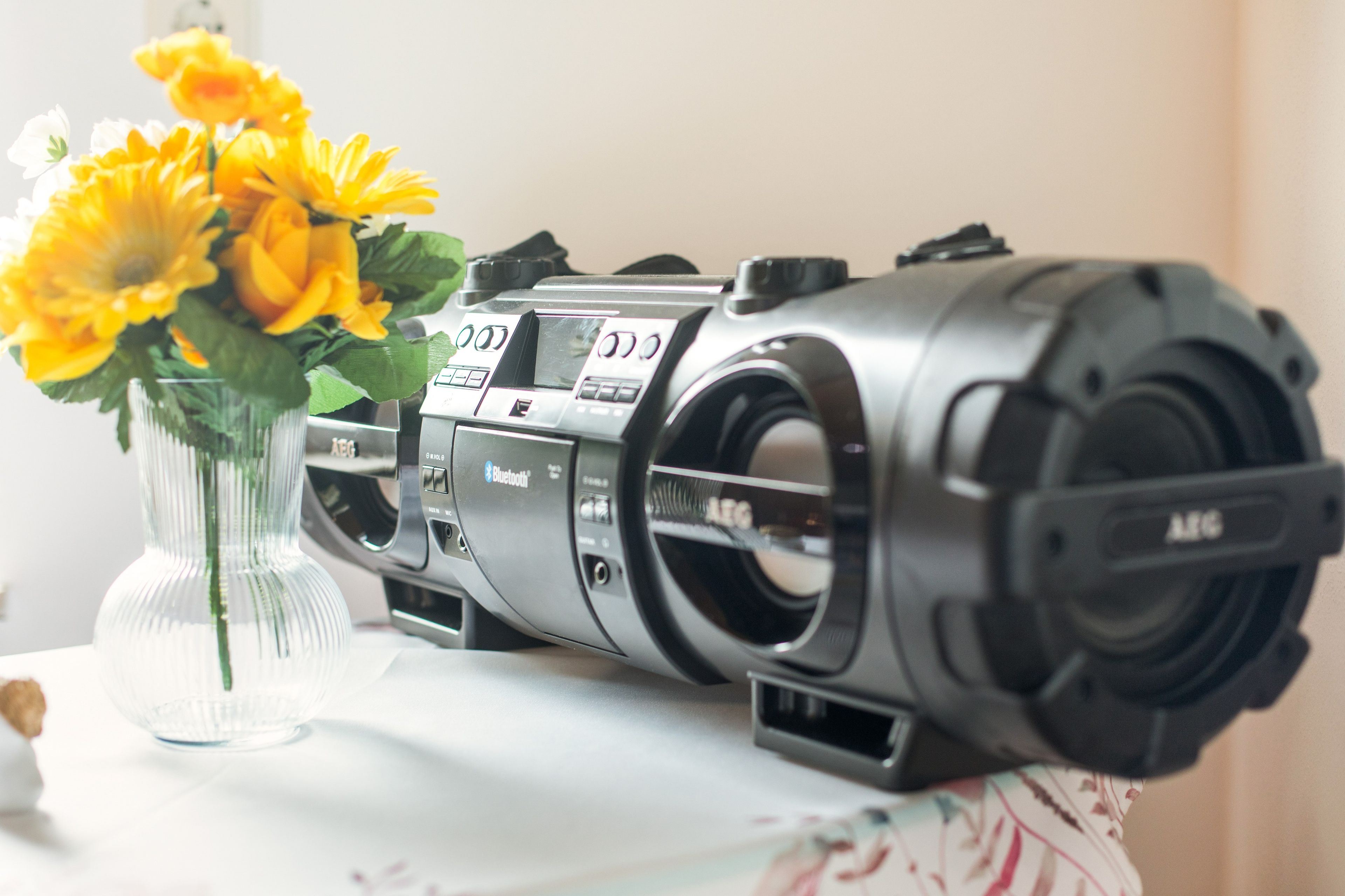 A vintage radio with a control panel and a vase with yellow flowers on a table.