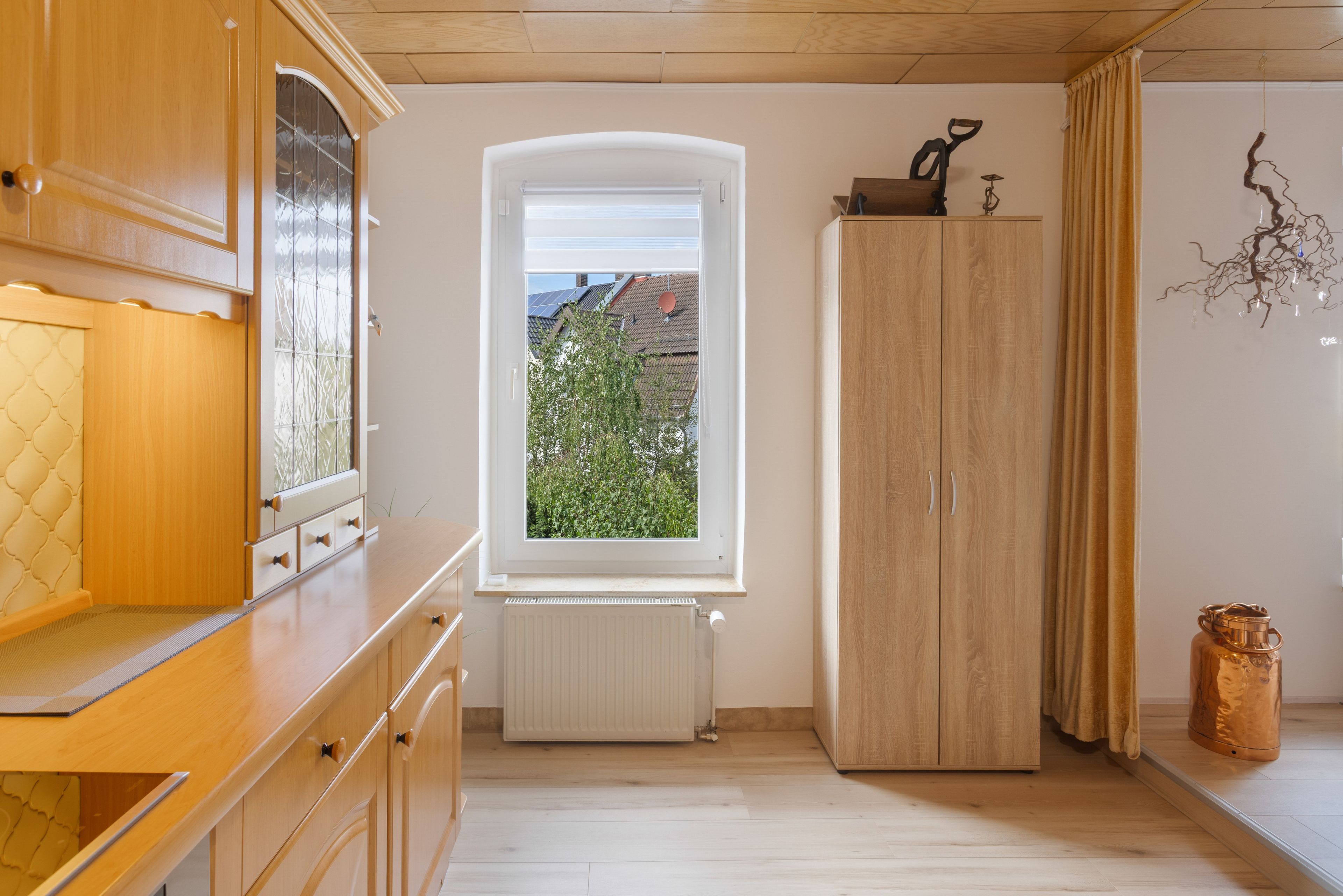 Et køkken med træskabe, et vindue med udsigt til grøn natur, og en radiator.