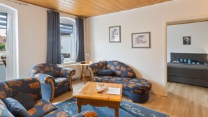 Een gezellige woonkamer met een houten plafond, een zithoek, een kleine tafel met een kaars, en een bed op de achtergrond.