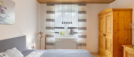 Une chambre à coucher avec un lit, une armoire en bois, un radiateur et une fenêtre avec des rideaux.