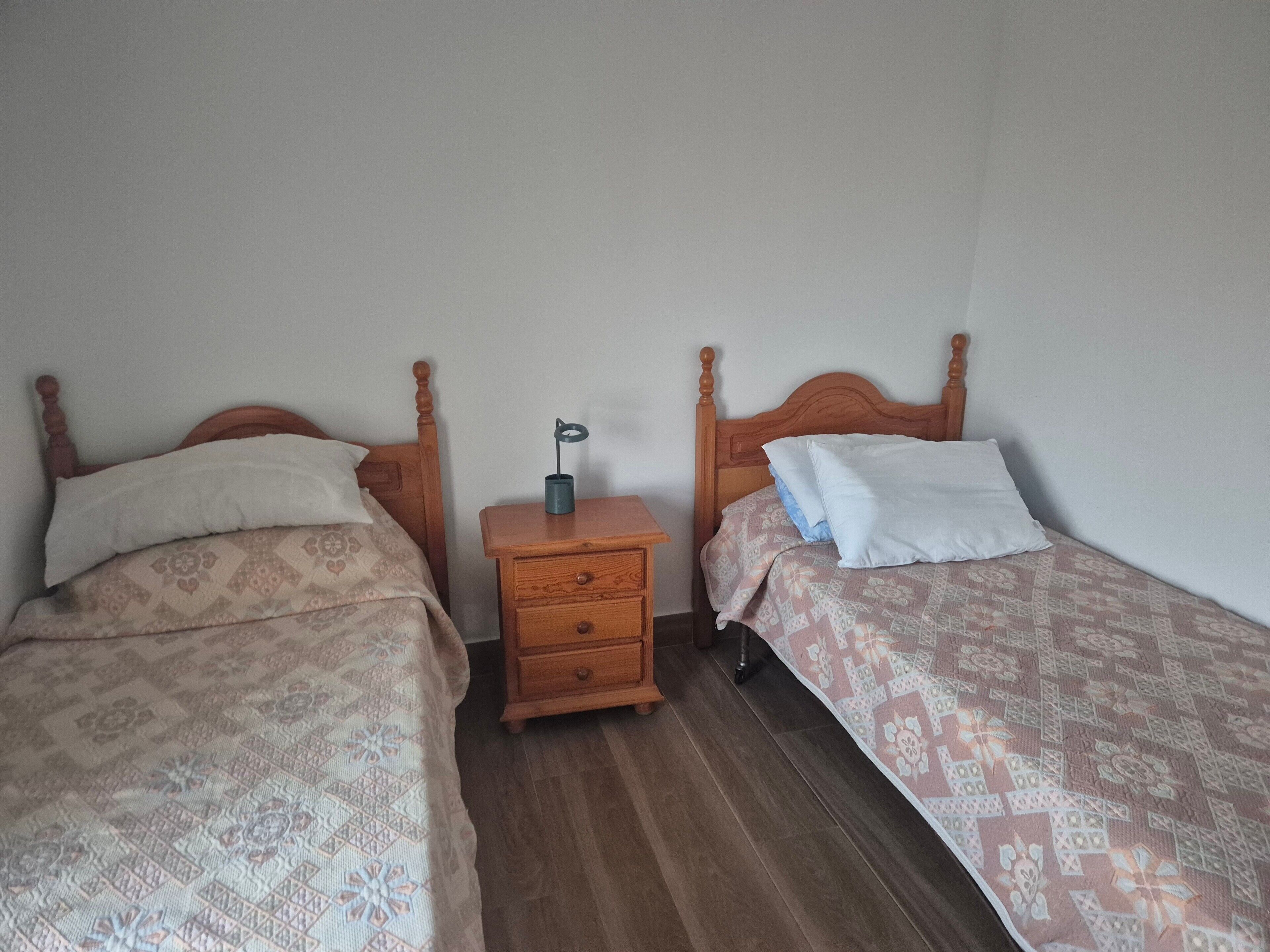 Two single beds with wooden headboards, a small wooden nightstand with a lamp, and a patterned bedspread.