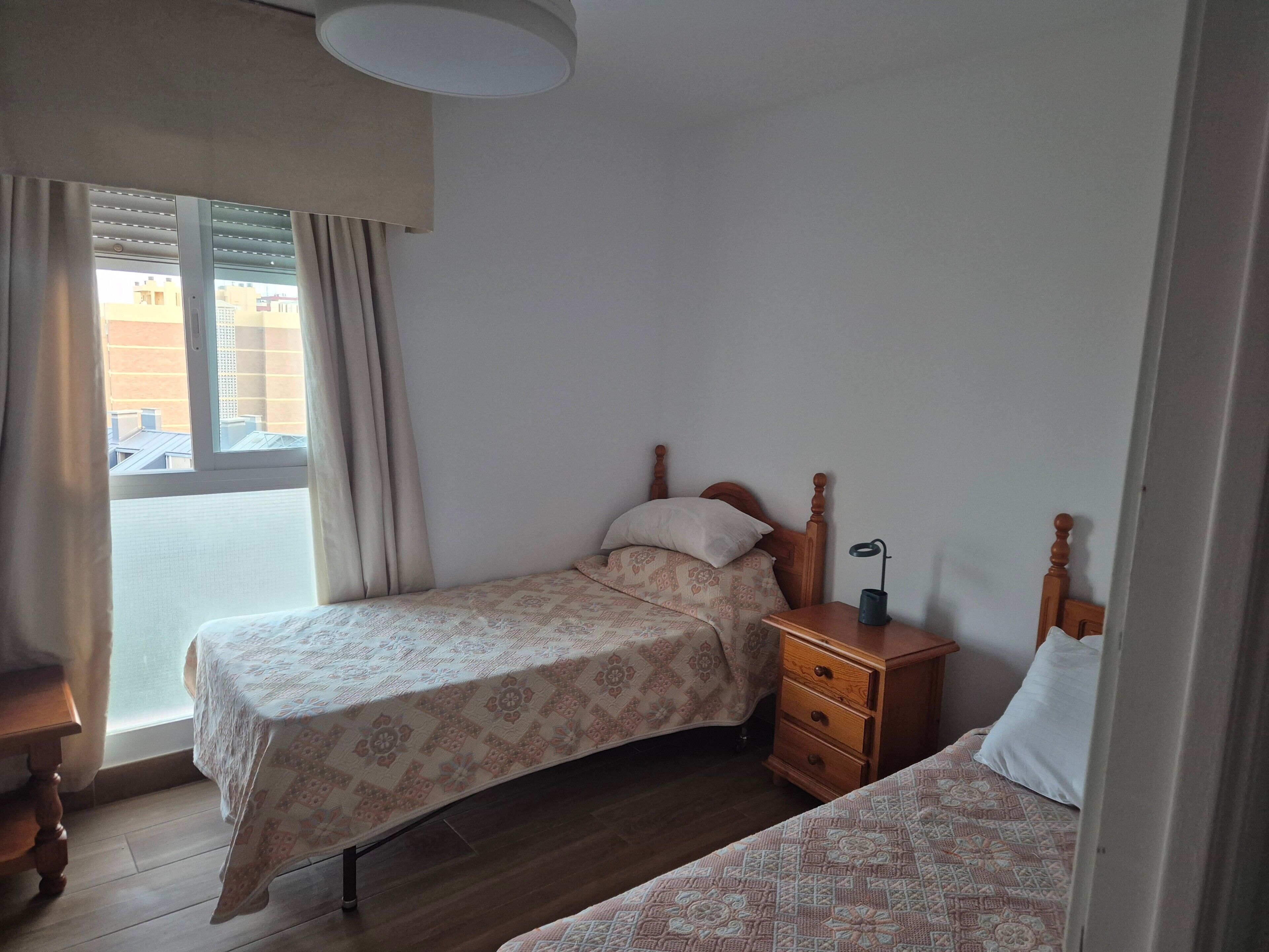 Ein Schlafzimmer mit zwei Betten, einem Nachttisch aus Holz, einem Beistelltisch und einem Fenster mit Vorhängen.