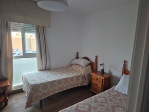 A bedroom with two beds, a wooden nightstand, a bedside table, and a window with curtains. - 'Pausa Azul' Apartment with Sea Views, Wi-Fi, and Air Conditioning (Benalmádena)