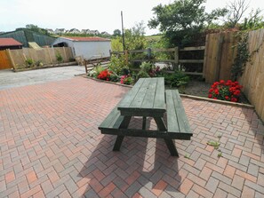 A picnic table in a brick-paved area with a wooden fence and flowering plants. - Coedllys Uchaf Cottage (Carmarthen)