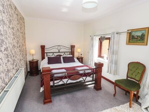 A bedroom with a four-poster bed, two bedside tables, a radiator, a window with curtains, a green upholstered chair, and a framed picture on the wall. - Coedllys Uchaf Cottage (Carmarthen)