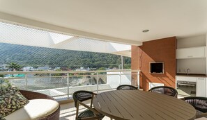 Ein Balkon mit Blick auf eine gebirgige Landschaft, Korbmöbel und ein eingebauter Grill.