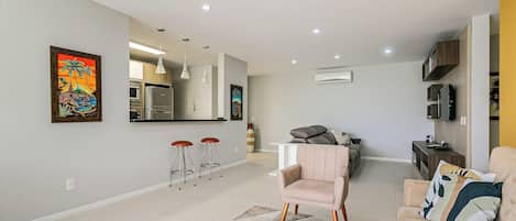 Una sala moderna con un sofá, una mesa de comedor y una zona de cocina con refrigerador y horno.