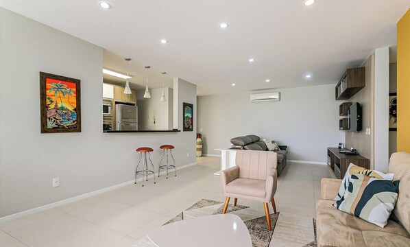 A modern living room with a sofa, a dining table, and a kitchen area with a refrigerator and oven. - Ap in Resort 200m From the Beach Floripa-sc Mhe003 (Florianópolis)