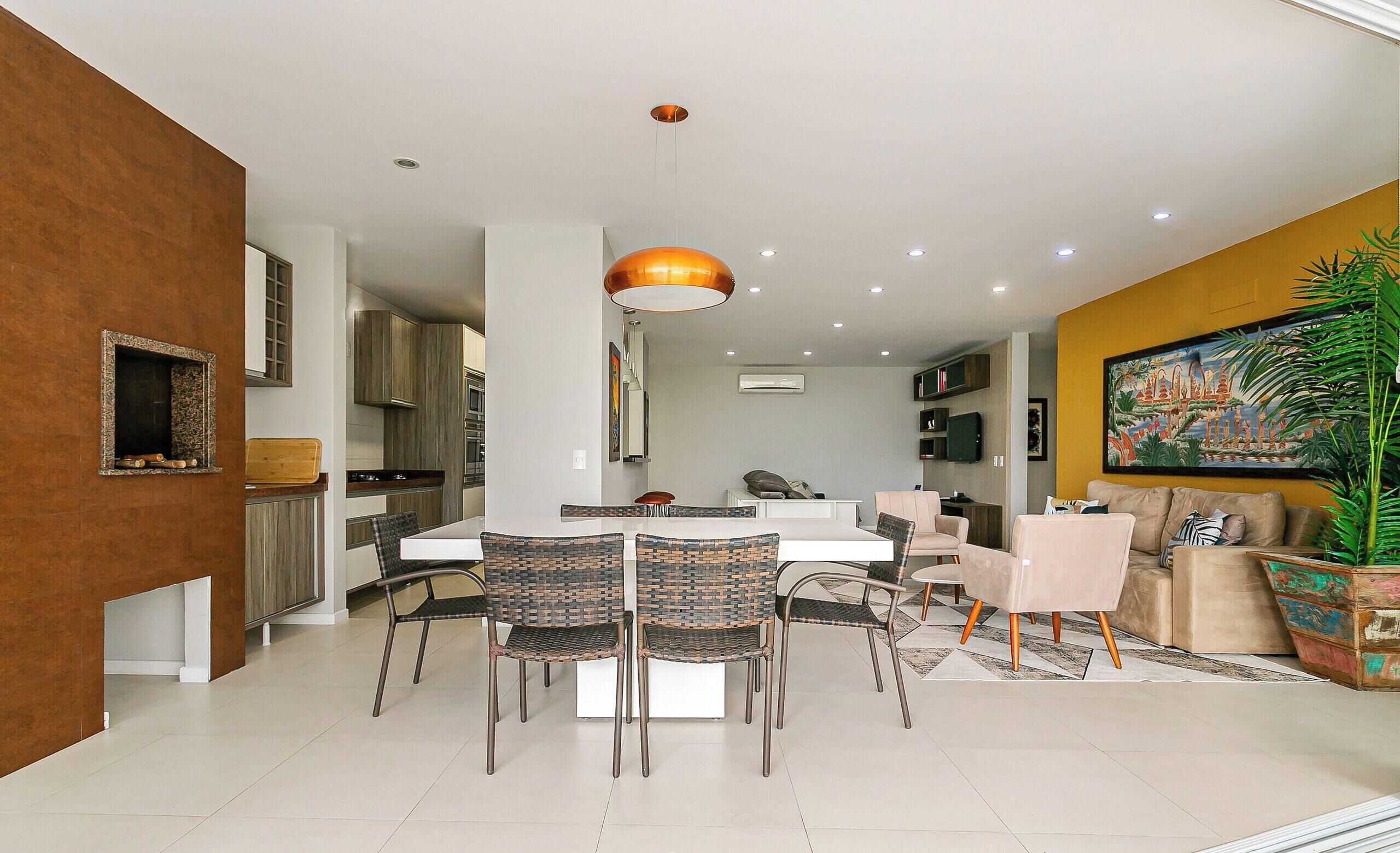Una cocina moderna con armarios blancos, un comedor con una mesa blanca y sillas de mimbre, y una sala de estar con un sofá y un cuadro grande.