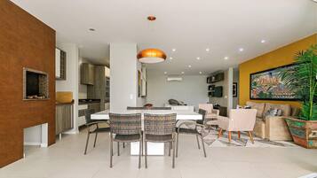 Una cocina moderna con armarios blancos, un comedor con una mesa blanca y sillas de mimbre, y una sala de estar con un sofá y un cuadro grande.