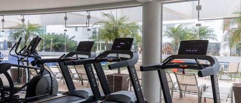 A gym with treadmills, exercise bikes, and a large window with a view of palm trees.