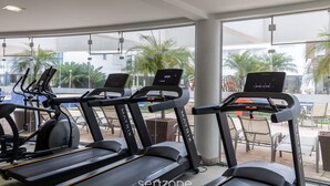 A gym with treadmills, exercise bikes, and a large window with a view of palm trees. - Ap in Resort 200m From the Beach Floripa-sc Mhe003 (Florianópolis)