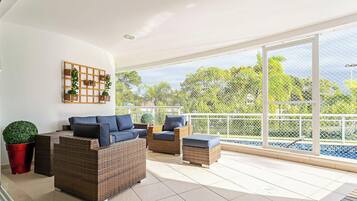 A spacious balcony with wicker furniture, a potted plant, and a view of greenery.