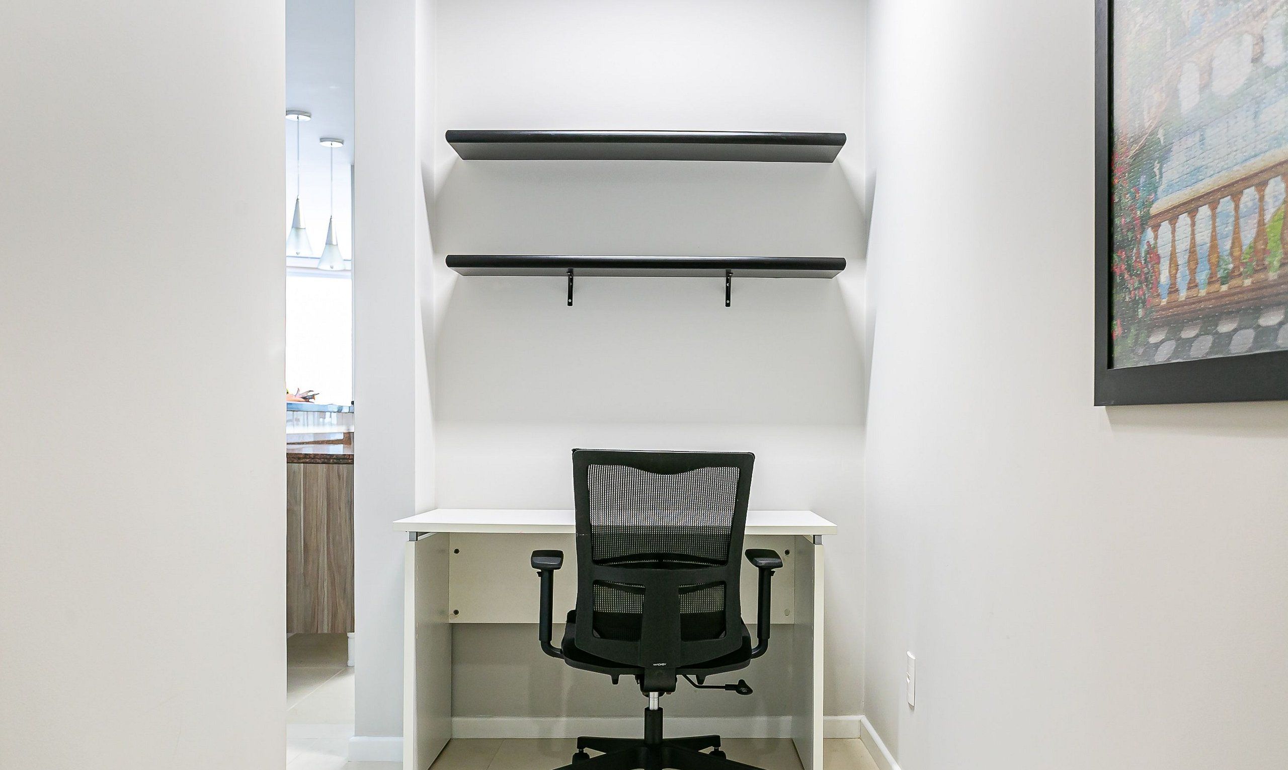 A modern office space with a desk, chair, and two wall-mounted shelves.