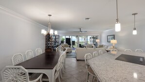 Un comedor espacioso con una mesa larga y sillas, una zona de cocina con encimera de mármol y vistas al exterior.