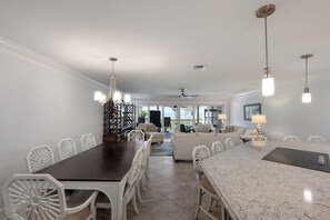 A spacious dining area with a long table and chairs, a kitchen area with a marble countertop, and a view of the outdoors. - Dunes of Boca 2 | 3 bedroom 3 Bath | Pool | Gulf Front | Tennis | Sleeps 6 (Boca Grande)