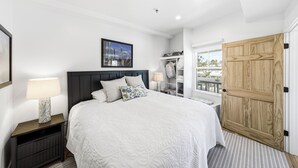 Un dormitorio con cama, mesitas de noche, una ventana y una puerta.