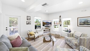 Un salón amplio con un sofá gris, sillones estampados, una mesa de centro de vidrio y un televisor.