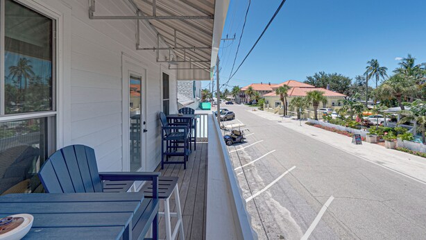 Un balcón con mobiliario exterior, con vistas a una calle con coches aparcados y palmeras.