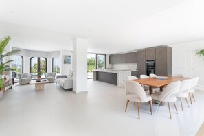 Un'ampia zona giorno con tavolo e sedie da pranzo, una cucina dotata di elettrodomestici moderni e ampie finestre con vista sul verde.