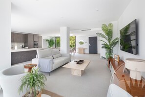 A modern living room with a white sofa, a coffee table, and a dining area with a table and chairs. - La Manga Club Individual Villa 619 (Atamaría)