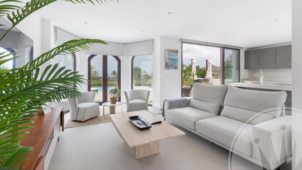 A modern living room with a sofa, chairs, a coffee table, and a view of a pool and mountains. - La Manga Club Individual Villa 619 (Atamaría)