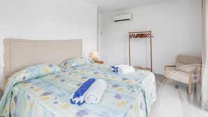 A hotel room with a large bed, a wooden chair, a hanging coat rack, and an air conditioning unit on the wall. - La Manga Club Individual Villa 619 (Atamaría)